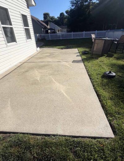 A concrete patio bordered by a white fence, adjacent to a well-maintained green lawn - before