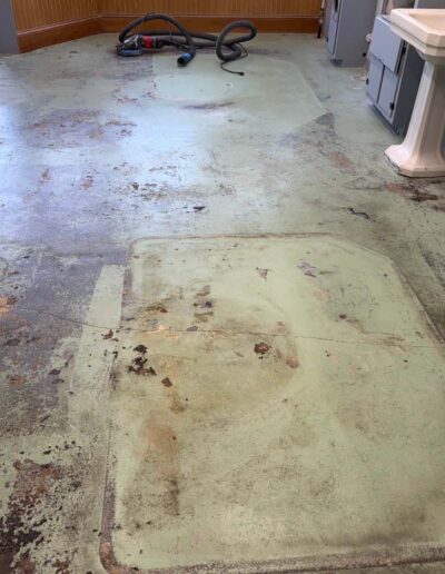 A worn, light green floor undergoes renovation, displaying patches of exposed concrete and outlines left by former equipment - www.shoreconcretecoating.com
